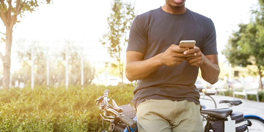 a man wearing a dark grey t-shirt and khaki pants using his smartphone while sitting on his bike